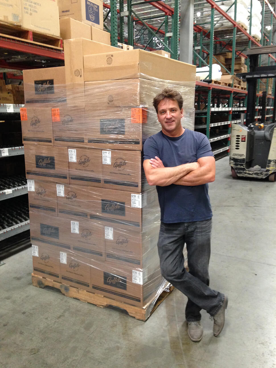 Tieman's Fusion Coffee owner standing in front of stacked product pallets in fulfillment warehouse
